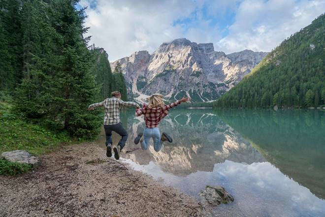 Young couple jumping mid-air by the mountain lake, Italy