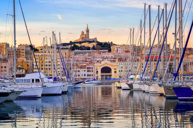 Yachts reflecting in the still water of the old Vieux Port of Marseilles beneath Cathedral of Notre Dame, France, at sunrise