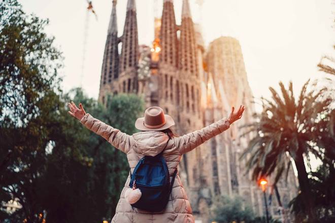 Rear view of young woman in front of Sagrada Familia with arms outstretched enjoying the beautiful city