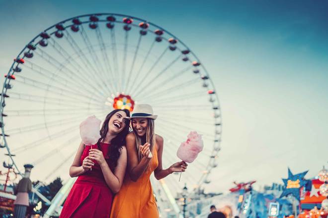 Two friends eating cotton candy and laughing at the amusement park